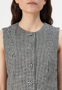 Svart och vit rutmönstrad klänning med rund halsringning, korta ärmar och tre dekorativa knappar framtill. Texturerat tyg.