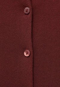 Burgunderfarbener Strickcardigan mit zwei runden Knöpfen und einem strukturierten Stoff. Nahaufnahme hebt die Nähte und die Details der Knöpfe hervor.