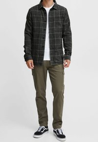 Czarna i szara koszula w kratę z guzikami i kieszenią, noszona na białym t-shircie. Zestawiona z oliwkowymi spodniami cargo i czarnymi sneakersami.