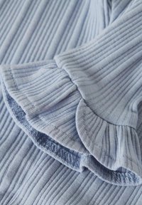 Jasnoniebieska dzianina prążkowana z rozkloszowanym rękawem wykończonym falbanką i elastycznym obszyciem, prezentująca miękką teksturę i subtelny połysk.