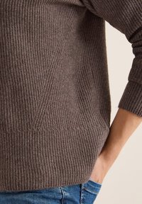 Brun ribbad stickad tröja med en boxig design, breda muddar och en texturerad yta. Detaljer inkluderar diagonala ribbmönster längs sidorna.