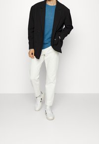 Schwarze doppelte Blazer, blauer Rundhalsausschnitt-Pullover, weiße tapered Hose, weiße Sneakers mit schwarzen Akzenten, minimalistisches Design, glatte Textur.