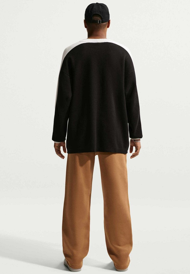 Pull à manches longues noir et blanc avec une coupe décontractée, associé à un pantalon ample couleur beige. Tissu texturé, design à épaule tombante et accents simples.