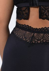 Sous-vêtements en dentelle noire ornés de motifs floraux complexes, avec une bordure texturée et une base en tissu lisse, mettant en valeur un design superposé.