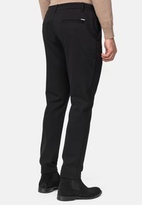 Pantalones negros de corte ajustado, hechos de una tela suave, con una cinturilla elástica, dos bolsillos traseros y sutiles acentos de hardware en plata.