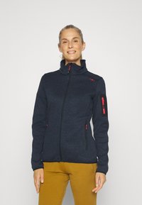 Navy fleece-takk med høy krage, har røde glidelåser og detaljer, to frontlommer og en lomme på ermet, teksturert stofffinish.