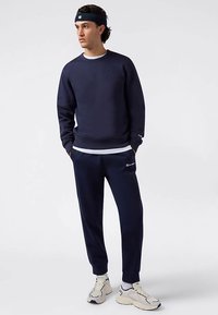 Granatowy zestaw bluzy i spodni z elastycznymi mankietami i pasem. Materiał z mieszanki bawełny, z akcentami logo i kontrastową białą warstwą pod spodem.