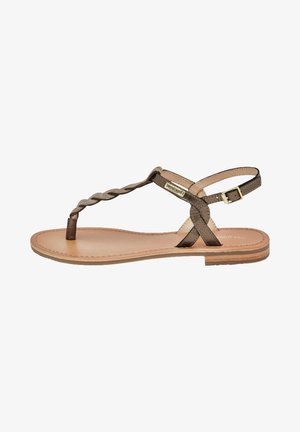 Sandale en cuir marron avec une lanière tressée au niveau des orteils, une sangle de cheville réglable, une semelle plate et un design minimaliste.