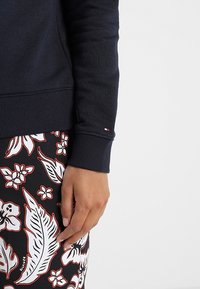 Felpa navy con polsini a costine; presenta un piccolo etichetta con logo. Abbinata a una gonna a fantasia con motivi floreali in nero, bianco e rosso.