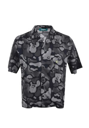 Camicia a maniche corte con bottoni, motivo astratto di teschi e ossa in nero, grigio e bianco, e una piccola faccina gialla sorridente sulla tasca del petto.