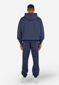 Mørkeblå hettegenser og joggebukse sett, med en avslappet passform, ribbestrikkede mansjetter og kengurulomme, kombinert med hvite sko.