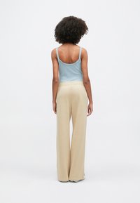 Ανοιχτό μπλε κορμάκι με λεπτές τιράντες και μπεζ παντελόνι φαρδιάς γραμμής, με απαλή υφή και άνετη εφαρμογή. Απλός, μινιμαλιστικός σχεδιασμός.