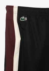 Svarta sportshorts med burgundy och creamfärgade sidopaneler, med en strukturerad väv och en grön och röd krokodil-logotyp på midjebandet.