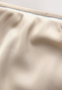 Beige tyg med en slät textur, som har subtila veck och en vit dragkedja längs övre kanten. Inga mönster eller prydnader syns.