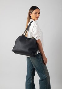 Black leather tote bag with textured finish, gold hardware accents, and sturdy shoulder straps. Features a roomy shape and flat base.