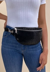 Black faux snake-skin fanny pack with a rounded shape, featuring a silver zipper and metal hardware, worn around the waist.