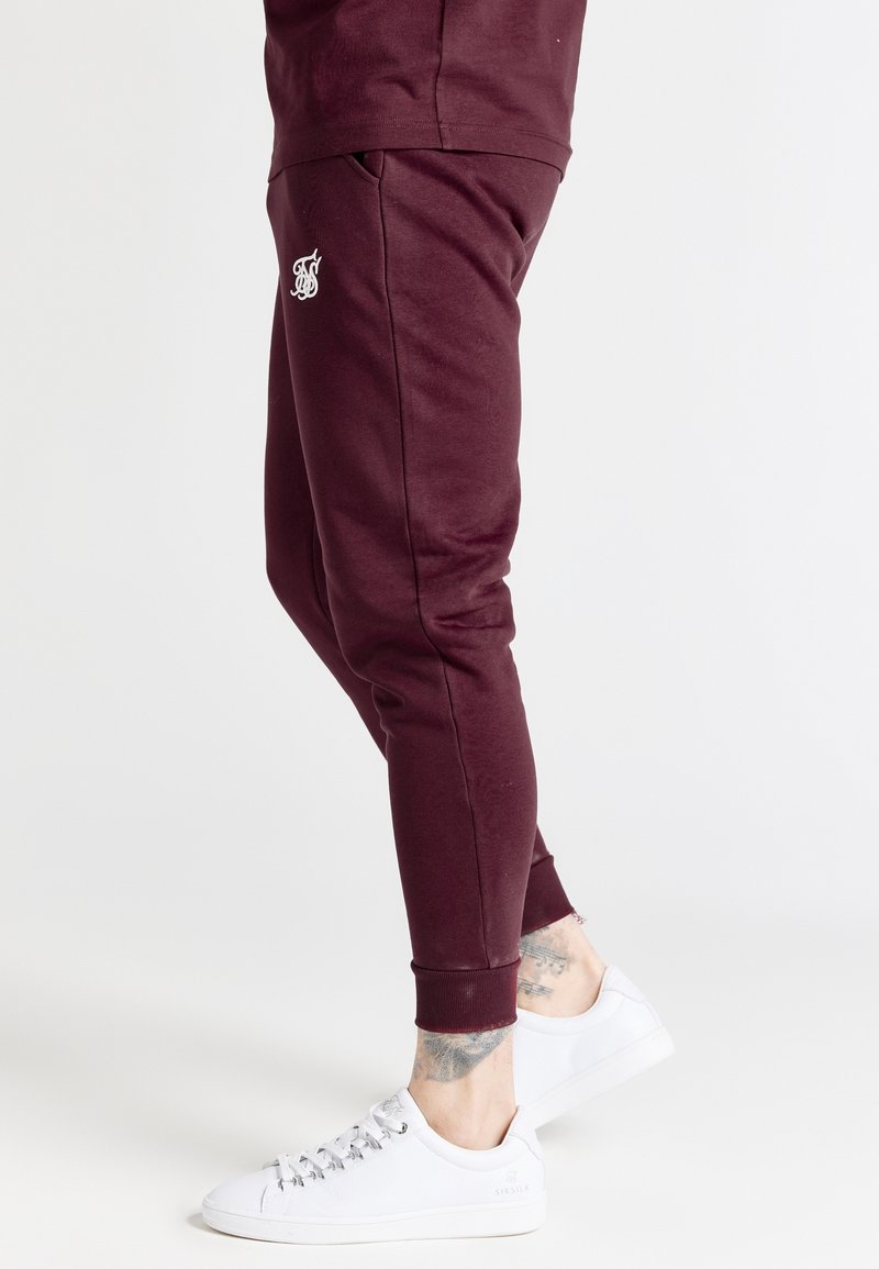 Bordeauxfärgade sweatpants i en bomullsblandning med elastiska muddar, sidofickor och vitt logodetalj. Matchade med vita sneakers för en komplett look.
