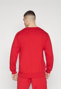 Rød genser med lange ermer, rund hals og ribbede mansjetter og kant. Laget av mykt materiale, med et enkelt, ensfarget design.