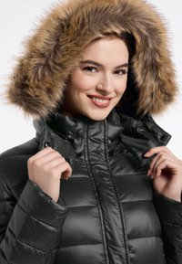 Donkergroene pufferjack met horizontale stiksels, een hoge kraag en een afneembare muts met bruine bontafwerking. Voorzien van drukknopen en een glanzende textuur.