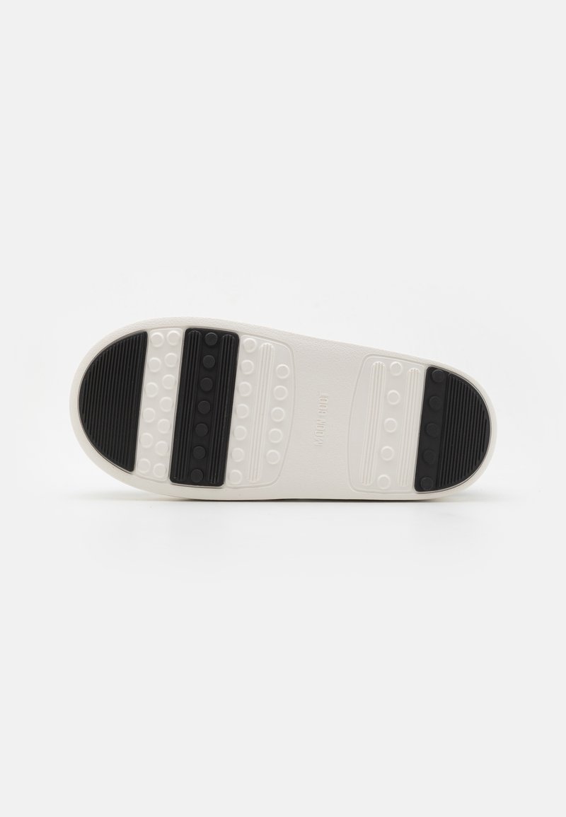 Weiße Schuhsohle mit schwarzen Gummielementen. Verfügt über strukturierte Grip-Bereiche und kreisförmige Muster. Flaches Design, glattes Material.