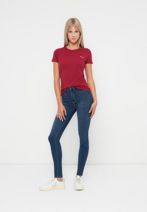 Rode, korte mouwen T-shirt met een ronde hals, gecombineerd met strakke blauwe jeans en witte sneakers met grijze accenten.