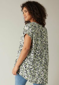 Blomsterbluse med et sort, hvidt og grønt mønster. Korte ærmer, løs pasform, rund bund og tekstureret stof. Kombineret med blå jeans.