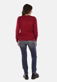 Maglione rosso a maniche lunghe con scollatura rotonda, abbinato a jeans blu scuro e stivali neri con piattaforma. Tessuto liscio e design aderente.