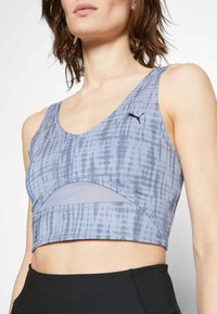 Brassière de sport bleu clair avec un motif tie-dye, dotée d'un panneau en mesh, d'un col arrondi et d'un logo noir. Confectionnée en tissu extensible.