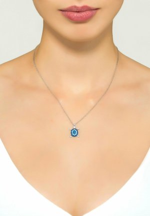 Silver necklace featuring a turtle-shaped pendant with blue gem accents and a round central stone, displayed on a bare neck.
