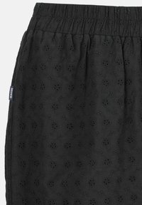 Gonna nera realizzata in tessuto testurizzato, caratterizzata da un motivo floreale ricamato e una linea vita elastica. Dettagli degni di nota includono piccoli intagli.