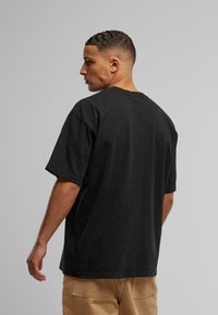 Svart bomullströja med avslappnad passform, korta ärmar och rund hals. Har en mjuk textur och minimala designinslag.