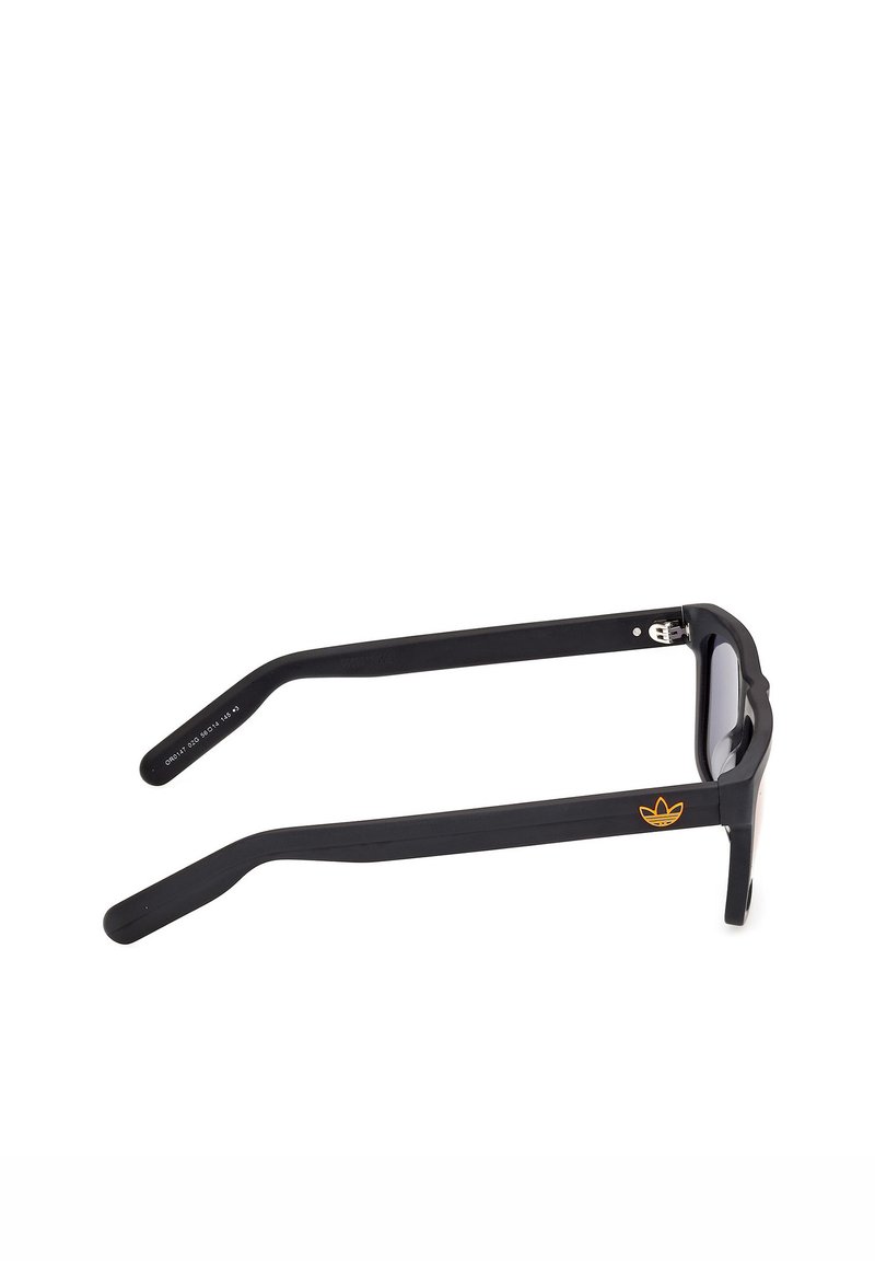 Gafas de sol rectangulares negras con montura gruesa, con un logo naranja de Adidas en la patilla, vistas desde un ángulo lateral.