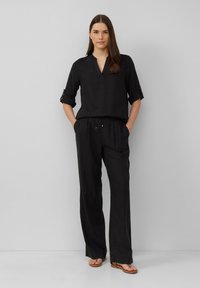 Zwarte linnen, lange mouwtop met een v-hals en opgerolde manchetten, gecombineerd met bijpassende losvallende broek met een elastische tailleband en een trekkoord.