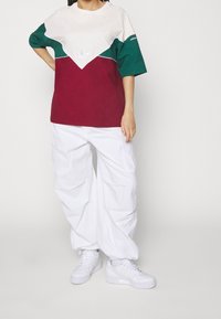 Färgglad t-shirt i kräm, grön och vinröd med en Adidas-logotyp. Kombinerad med lösa vita cargobyxor och vita sneakers.