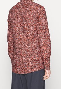Camicia a maniche lunghe con un motivo floreale rosso, bianco e nero. Realizzata in tessuto leggero, presenta un colletto classico e polsini con bottone.