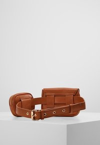 Ruskea nahkavyölaukku kahdella kiinnitetyllä pussukalla, kultainen solki ja ompeluominaisuudet, esillä valkoisella jalustalla yksiväristä harmaata taustaa vasten.