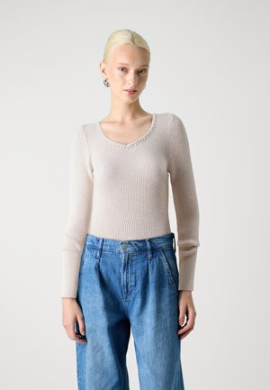 Light beige ribbed sweater with a V-neck and long sleeves, paired with high-waisted blue denim trousers with wide legs and pleats.
