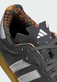 Basket noire et grise avec un dessus texturé, doublure orange à motifs, rayures blanches et une semelle en caoutchouc distinctive avec des lacets.