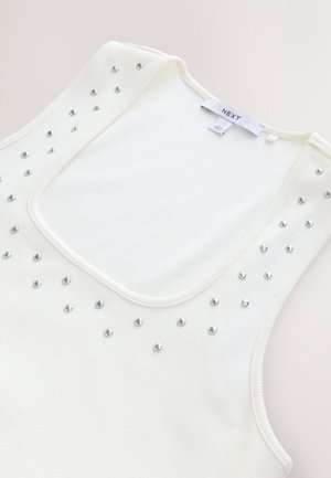 Biały prążkowany top na ramiączkach z szerokim dekoltem, ozdobiony srebrnymi ćwiekami z przodu, zaprojektowany na dopasowaną sylwetkę.
