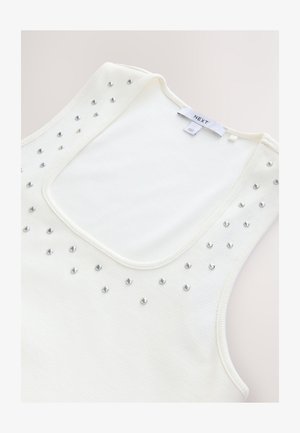 Vit ribbad linne med vid halsringning, prytt med silvernitar över framsidan, designad för en figurnära siluett.