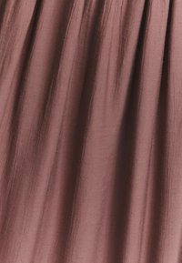 Tekstureeritud kangas pehmelt mauve värvitoonis, voolates pehmete, hõljuvate kortsudega ja siledal pinnal.