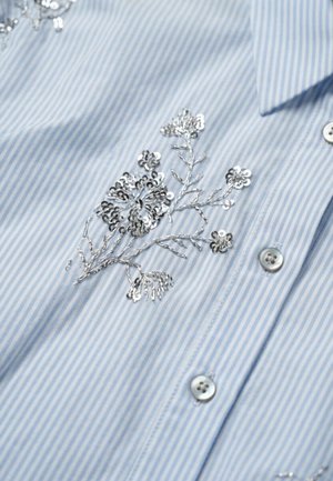 Lichtblauw-wit gestreept overhemd met zilveren pailletten bloemenborduursel bij de knopen en kraag.