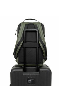 Maleta de ruedas negra con una mochila de textura verde oscura asegurada en la parte superior. La mochila cuenta con malla acolchada y correas ajustables para mayor comodidad.