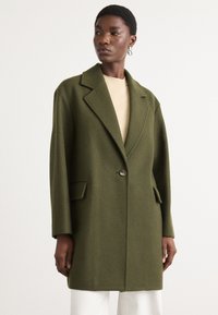 Olive green wool blend coat with a tailored design, large notched lapels, a single button closure, and side pockets. Smooth texture.