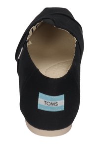 Scarpe slip-on in tela nera con punta rotonda, dotate di un'etichetta blu con la scritta "TOMS" sul tallone e di una soletta testurizzata.