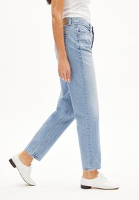 Jeans in denim blu chiaro con taglio dritto, dotati di un classico design a cinque tasche e vita media. Indossati con scarpe bianche.