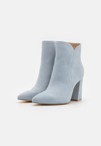 Botas de ante azul claro hasta el tobillo con punta afilada y tacón ancho. El diseño presenta una textura suave y una abertura en forma de V en la parte superior.