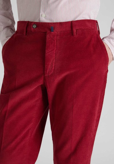 Rote Cord-Hosen mit vertikalen Rippstrukturen, ausgestattet mit einem Reißverschluss und einem Knopfverschluss, sowie Seitentaschen. Die Textur wirkt weich und robust.