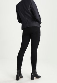 Svarta slim fit-jeans med ett slitet mönster, ihopkopplade med en strukturerad mörk jacka. Svarta ankelstövlar med blockklack och detaljer med sidogångjärn.