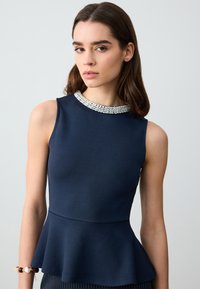 Top peplum blu navy senza maniche, con scollatura decorata con perline e tessuto testurizzato. Accentuato da una vita aderente e orlo svasato.
